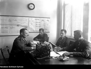 Policjanci podczas służby. Na stole widoczna maszyna do pisania, w tle na ścianie plansze przedstawiające budowę karabinka Mosin wz. 919825