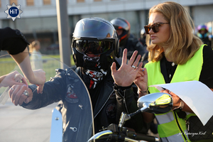 Motocyklista w kasku siedzi na motocyklu. Obok niego kobieta w odblaskowej kamizelce z kartka w ręku.
