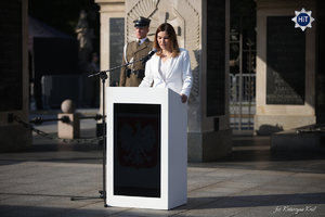 Przy pomniku Nieznanego Żołnierza w Warszawie stoi kobieta i przemawia do mikrofonu stojąc przy mównicy.