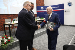 Jeden z zaproszonych gości mający na przedramieniu biało-czerwona powstańcza opaskę otrzymuje pamiątkową książkę oraz gratulacje od prelegenta.