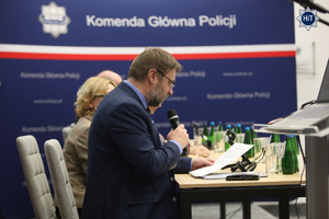 Przy prezydialnym stole siedzą prelegenci. W tle granatowy roll-up z napisem ‘Komenda Główna Policji”.