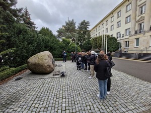 Uczniowie stoją przed obeliskiem. Za nimi budynek Komendy Głównej Policji.