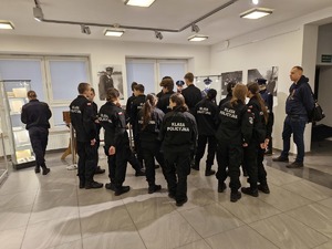 Młodzież z klasy mundurowej stoi w holu Wydziału Edukacji Historycznej. Na plecach granatowych mundurów widnieje napis: „ klasa policyjna”.
