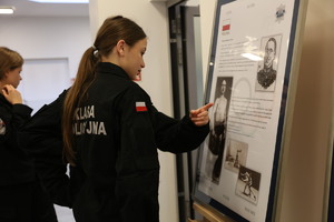 Uczennice klasy mundurowej czytają materiały umieszczone na sztalugach i oprawione w ramy.