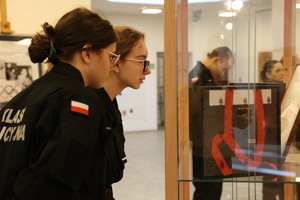 Uczennice klasy mundurowej oglądają eksponaty w gablotach.