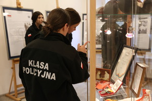 Uczennice klasy mundurowej oglądają eksponaty umieszczone w gablotach.