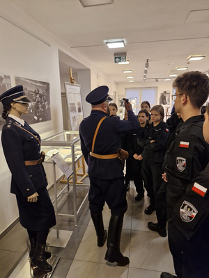 Pracownik Wydziału ubrany w mundur funkcjonariusza Policji Państwowej oprowadza uczniów po wystawie.
