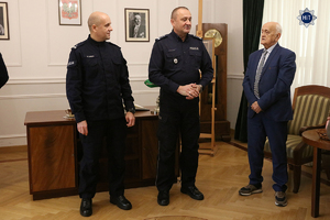 Insp Robert Żółkiewski – Dyrektor Gabinetu Komendanta Głównego Policji, funkcjonariusz Policji oraz trener piłkarski Andrzej Strejlau stoją w zrekonstruowanym gabinecie Komendanta Głównego Policji