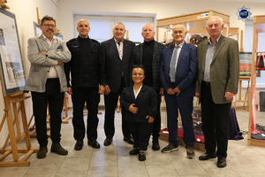 Olimpijczycy wraz z pracownikami Wydziału Edukacji Historycznej stoją w jednej z sal gdzie prezentowana jest wystawa. W tle gabloty i sztalugi z archiwalnymi zdjęciami