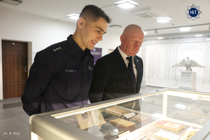Funkcjonariusz Policji oraz insp. w st. spocz. Andrzej Kuczyński  oglądają eksponaty prezentowane w gablotach w Wydziale Edukacji Historycznej.