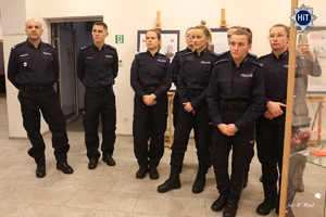 Grupa funkcjonariuszek Policji – reprezentantek drużyny w Futsalu stoi w holu budynku Wydziału Edukacji Historycznej i słucha oprowadzającego po wystawie. W tle gabloty z eksponatami.
