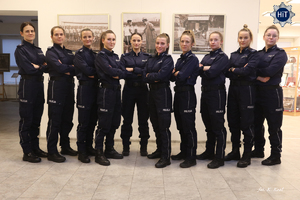 Reprezentantki drużyny w Futsalu stoją w rzędzie i pozują do zdjęcia na tle archiwalnych fotografii prezentowanych w Wydziale Edukacji Historycznej.