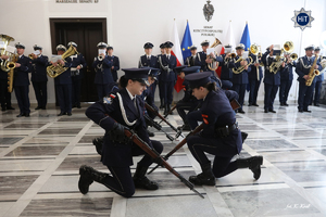 Orkiestra reprezentacyjna polskiej Policji gra w holu Senatu. Przed nią policjantki wykonują pokaz musztry ze strzelbami strzeleckimi.