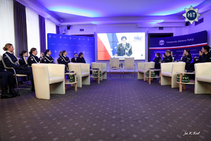 Policjantki uczestniczą w zdalnej konferencji. Z ekranu przemawia funkcjonariuszka Policji. Po prawej stronie ściana z policyjną gwiazdą i napisem Komenda Główna Policji.