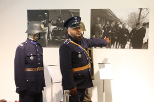 Policjant ubrany w mundur funkcjonariusza Policji Państwowej prezentuje policjantom archiwalne zdjęcia znajdujące się na wystawie