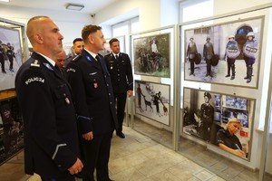 Funkcjonariusze Policji przyglądają się zdjęciom prezentowanym na jednej ze ścian.