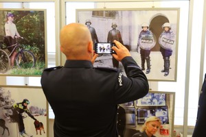 Funkcjonariusz Policji robi zdjęcie telefonem komórkowym fotografiom prezentowanym na wystawie.