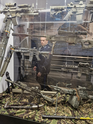 Funkcjonariusz Policji stoi przy gablocie, w której prezentowana jest broń.