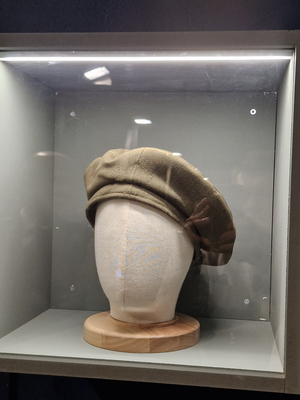 W podświetlanej szklanej witrynie prezentowany jest żołnierski beret.