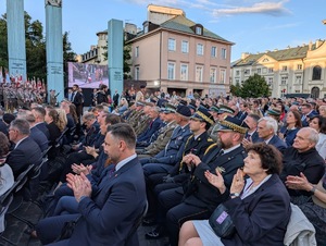 Widok na zaproszonych gości siedzących przed Pomnikiem Powstańców Warszawskich.