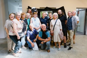 Grupa uczestników wycieczki pozuje do wspólnego zdjęcia w holu Wydziału Edukacji Historycznej. W środku stoi funkcjonariuszka Policji.