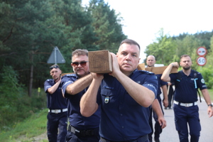 Funkcjonariusze Policji niosą na ramionach wielki drewniany prawosławny krzyż.