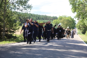 Funkcjonariusze Policji niosą na ramionach wielki drewniany prawosławny krzyż. Za nimi idą górnicy w odświętnych strojach oraz uczestnicy pielgrzymki.