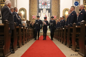 Funkcjonariusze Policji idą środkiem Kościoła niosąc sztandar. W ławkach stoją funkcjonariusze Policji oraz osoby uczestniczące we Mszy Św.