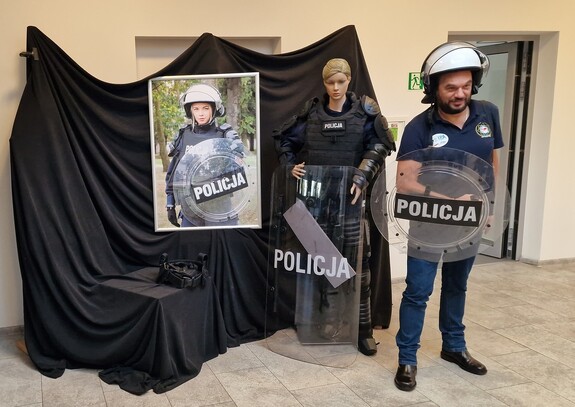 Mężczyzna pozuje trzymając policyjną tarczę obronną stojąc obok