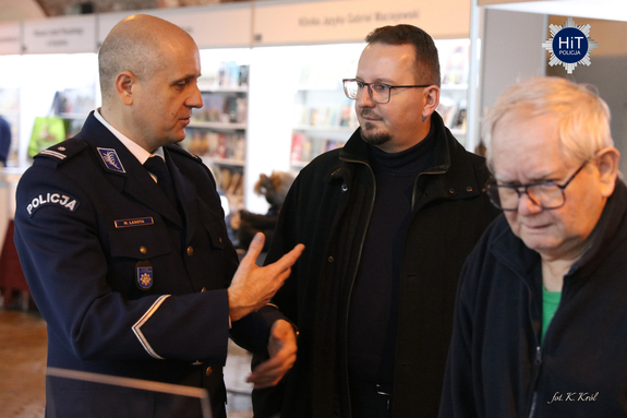 Funkcjonariusz Policji rozmawia z mężczyznami odwiedzającymi stoisko Wydziału Edukacji Historycznej.