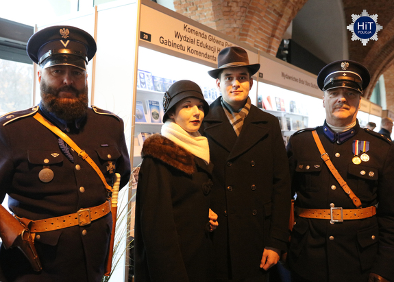 Kobieta z mężczyzną pozują do wspólnego zdjęcia z dwoma mężczyznami w umundurowaniu funkcjonariuszy Policji Państwowej.