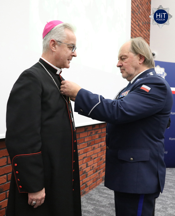 Funkcjonariusz Policji przypina odznaczenie księdzu biskupowi.