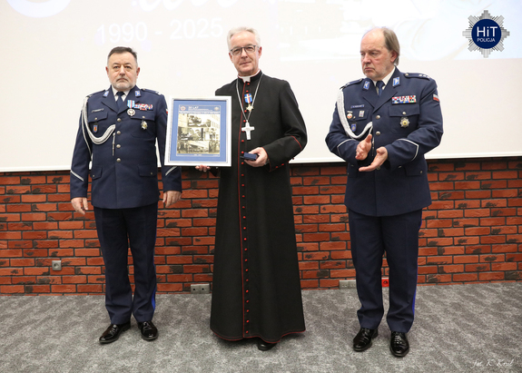 Ksiądz biskup prezentuje zebranej publiczności otrzymane odznaczenie oraz pamiątkową tablice