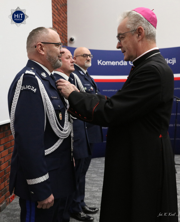 Ksiądz biskup przypina odznaczenia funkcjonariuszom Policji.