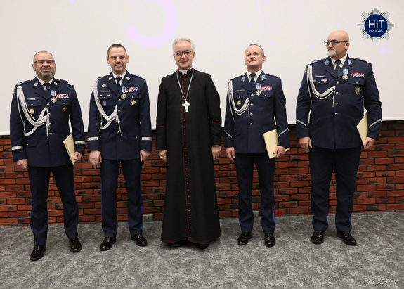 Ksiądz biskup pozuje do wspólnego zdjęcia z policjantami, którzy otrzymali honorowe odznaczenie.