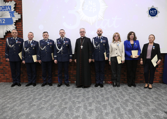 Ksiądz biskup pozuje do wspólnego zdjęcia z policjantami i pracownikami cywilnymi, którzy otrzymali honorowe odznaczenie.