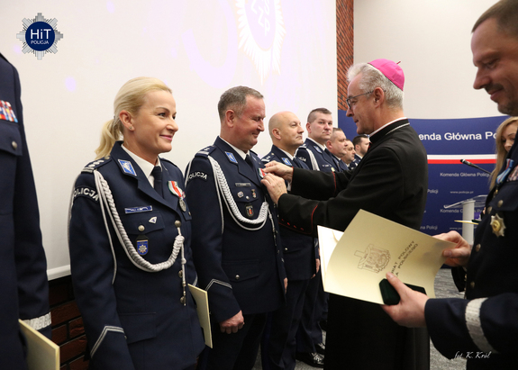 Ksiądz biskup przypina odznaczenia funkcjonariuszkom i funkcjonariuszom Policji.