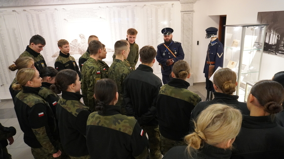 Uczniowie klasy mundurowej uczestniczą w oprowadzaniu po wystawie przed pracownika Wydziału ubranego w mundur funkcjonariusza Policji Państwowej