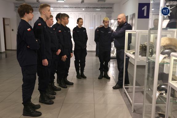 Kilku uczniów z klasy mundurowej stoi przed gablotami w holu Wydziału Edukacji Historycznej