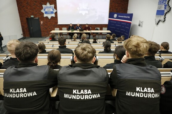 Na sali wykładowej siedzą uczniowie z klasy mundurowej. Przed nimi prelegenci prowadzący wykład