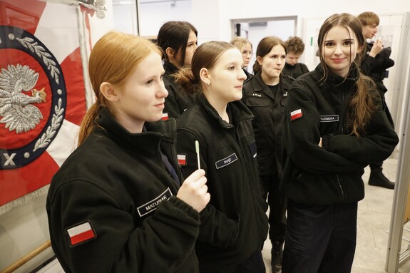 Uczennice klasy mundurowej stoją obok sztandaru z wizerunkiem orła