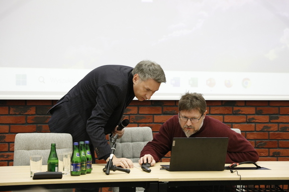 Dwóch prelegentów prowadzących wykład pochyla się nad komputerem