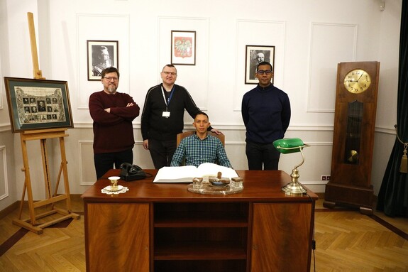 Czterech mężczyzn pozuje do zdjęcia grupowego w zrekonstruowanym Gabinecie Komendanta Głównego Policji Państwowej.