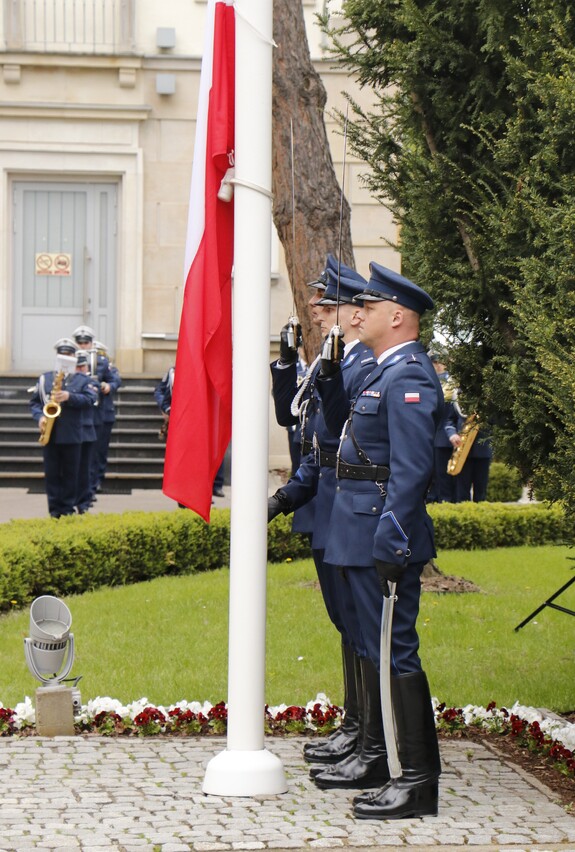 Policjanci podczas uroczystego wciągania flagi biało czerwonej na maszt trzymają szable kierowane ku górze