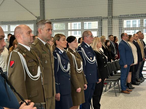Oficerowie Wojska Polskiego, policjanci a także zaproszeni goście stoją na sali, w której odbywa się uroczystość